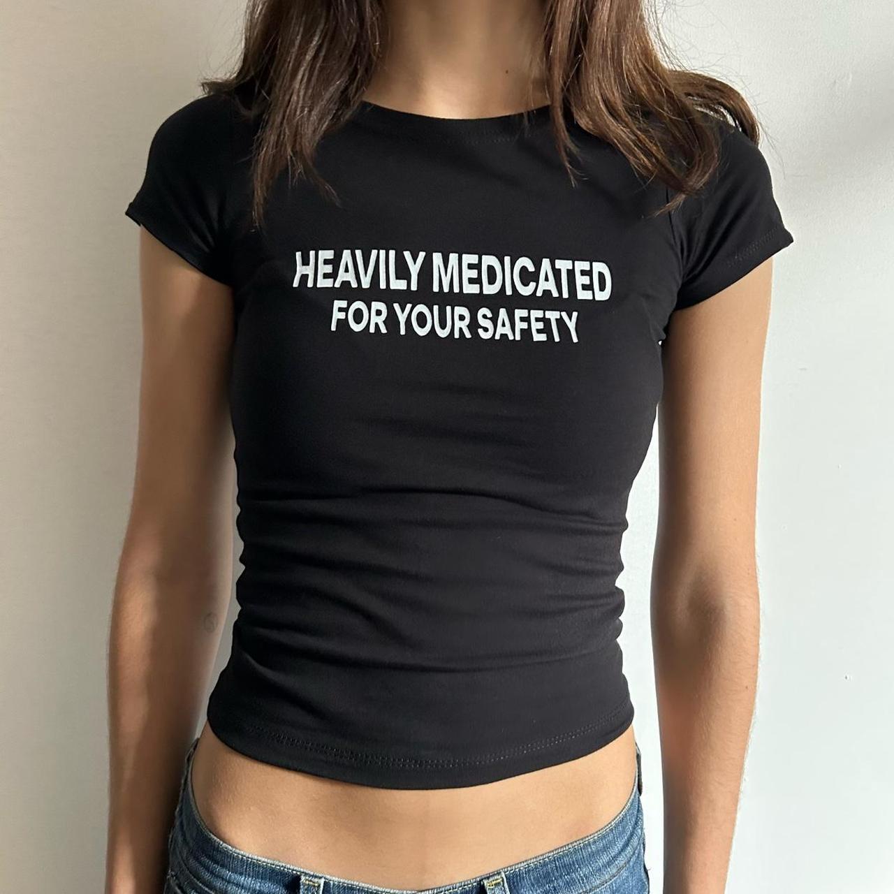 Model wearing black baby tee with "Heavily Medicated For Your Safety" written in white across the chest.