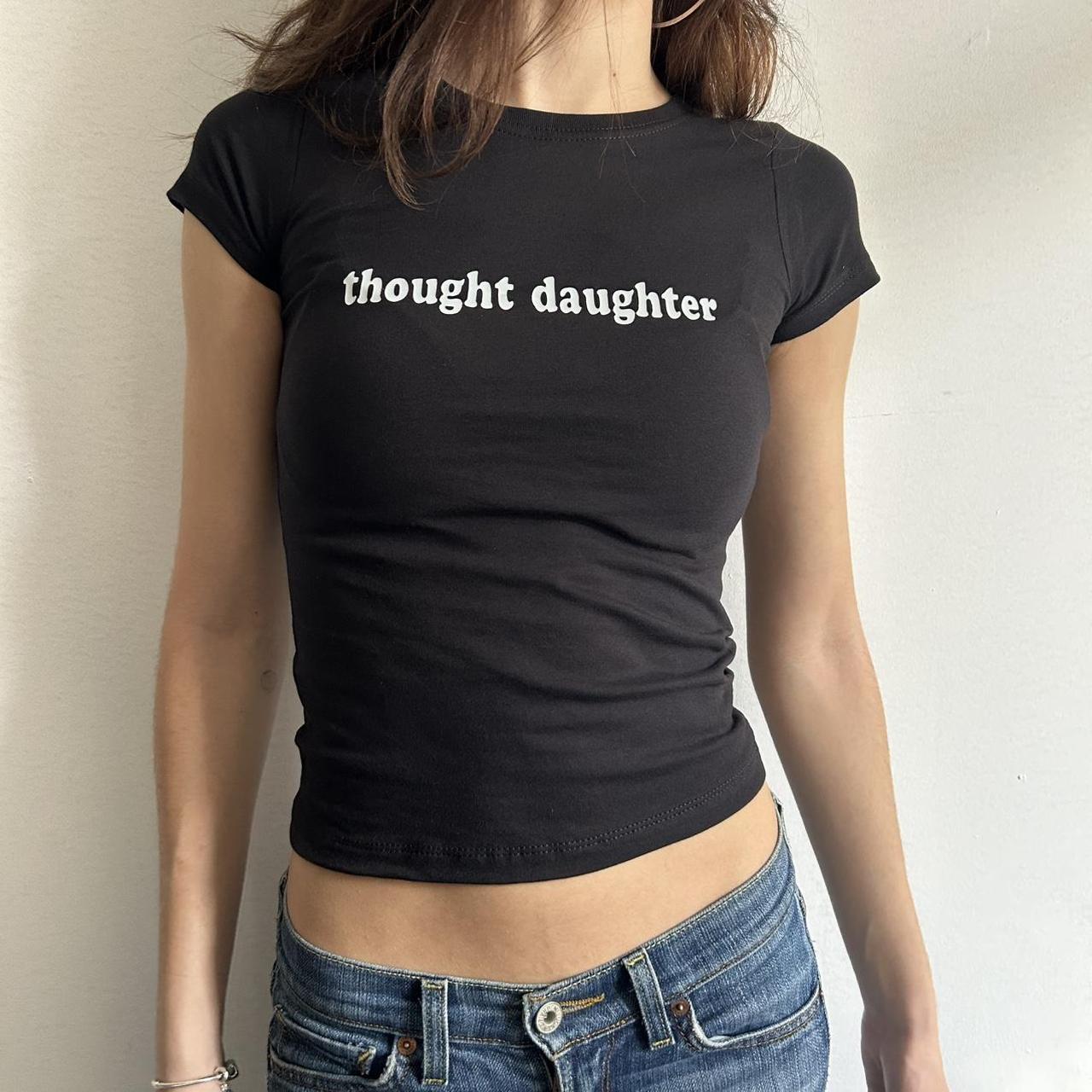 Model wearing black baby tee with "Thought Daughter" written in white across the chest.