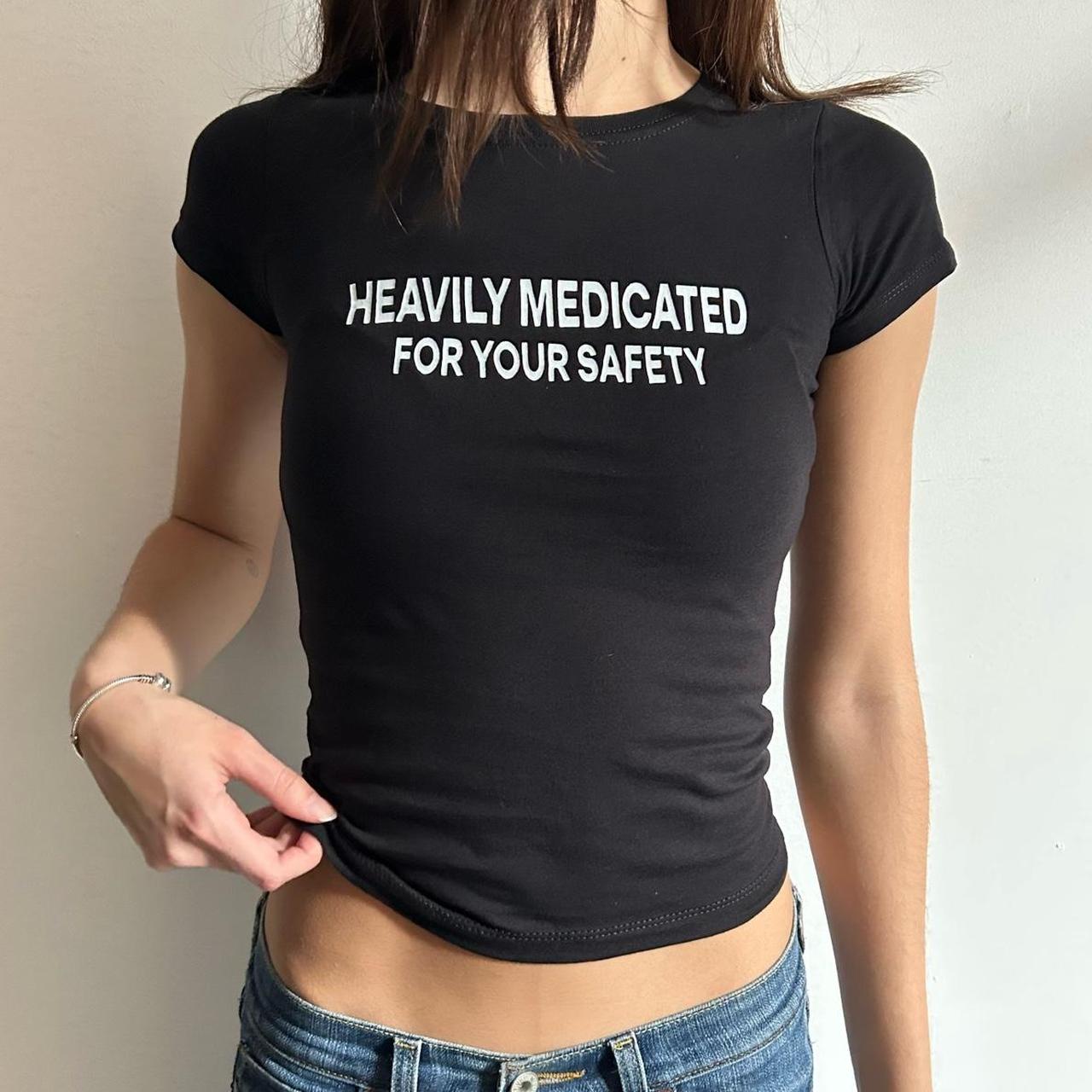 Model wearing black baby tee with "Heavily Medicated For Your Safety" written in white across the chest.