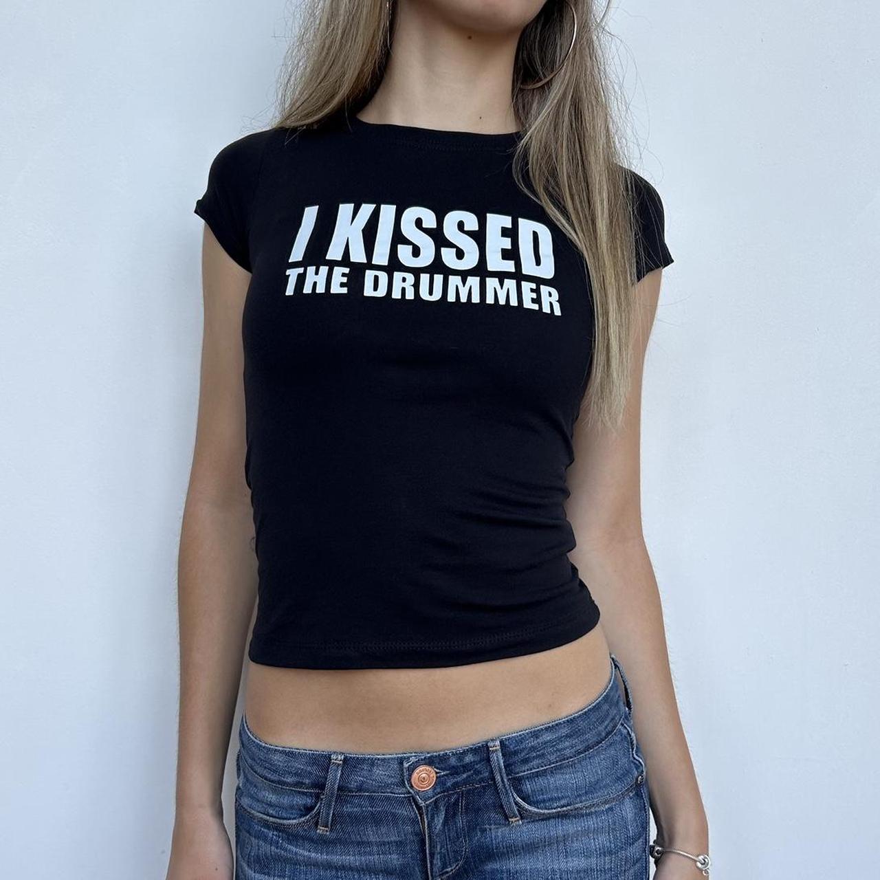 Model wearing black baby tee with "I Kissed The Drummer" written in white across the chest.
