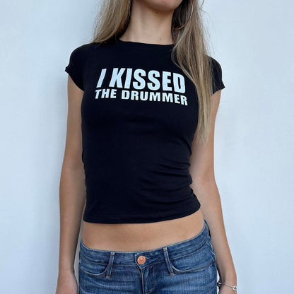 Model wearing black baby tee with "I Kissed The Drummer" written in white across the chest.