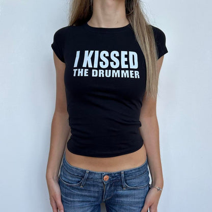 Model wearing black baby tee with "I Kissed The Drummer" written in white across the chest.