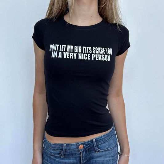 Model wearing black baby tee with "Don't Let My Big Tits Scare You, I'm A Very Nice Person" written in white across the chest.