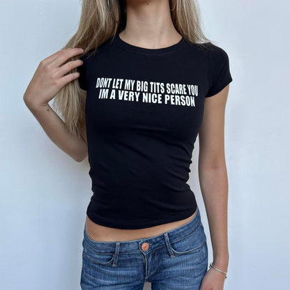 Model wearing black baby tee with "Don't Let My Big Tits Scare You, I'm A Very Nice Person" written in white across the chest.