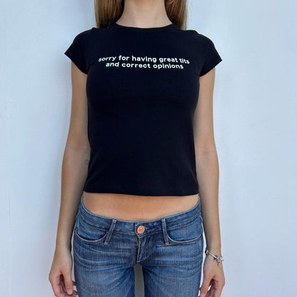 Model wearing black baby tee with "Sorry for Having Great Tits and Correct Opinions" written in white across the chest.