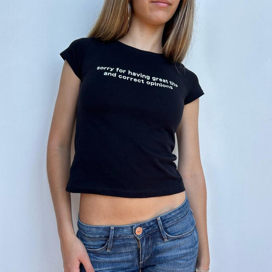 Model wearing black baby tee with "Sorry for Having Great Tits and Correct Opinions" written in white across the chest.