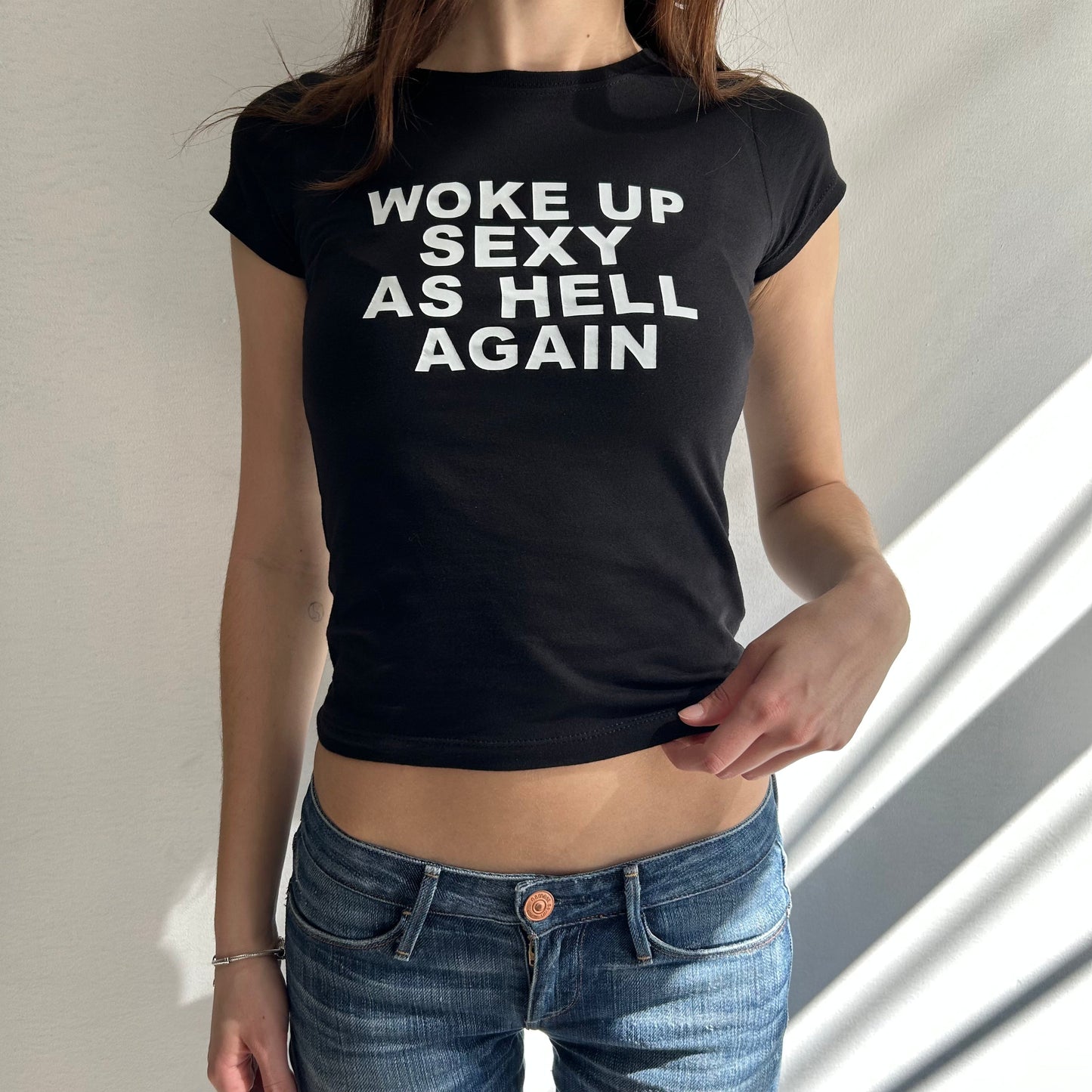 Model wearing black baby tee with "Woke Up Sexy As Hell" written in white across the chest.