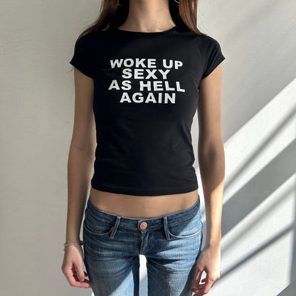 Model wearing black baby tee with "Woke Up Sexy As Hell" written in white across the chest.